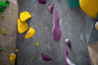 Spor salonundaki gri duvara tırmanma tutuşu. Renkli kulplu yapay kaya tırmanma duvarı.. 