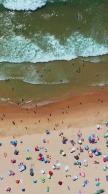 Yüzmek ve güneşlenmek gibi yaz etkinliklerinin tadını çıkaran insanlarla dolu kumlu bir sahil manzarası. Sahne, sahile gidenlerin dinlenip eğlendiği canlı bir okyanus günü yakalıyor.