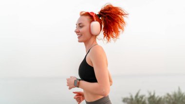 Mutlu sporcu kadın açık havada deniz manzarasına karşı koşuyor. Spor giyim kuşağında kadın müzik dinlerken gündüzleri egzersiz yapıyor.. 
