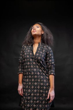 Siyah arka planda duran geleneksel siyah kurta giyen düşünceli kadın. Vitiligo deri bozukluğu olan düşünceli genç bir kadın stüdyoya bakıyor.. 