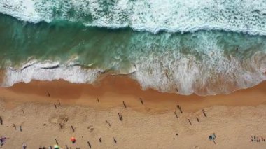 Kumlu sahildeki isimsiz turistler, dalgaların gün içinde plajda usulca dalgalanarak huzurlu ve manzaralı sahil ortamının keyfini çıkarırken, 