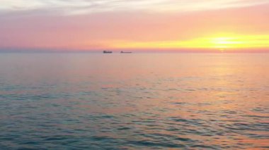 Durgun sularla kaplı cennet gibi deniz manzarası bulutların gökyüzüne doğru uzanıp ufuk çizgili sakin ve resimsel bir sahne oluşturmasıyla günbatımını yansıtıyor.