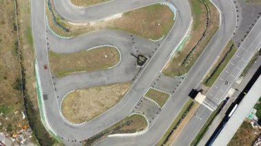 Havadan bakıldığında, go-kart 'ların dolambaçlı yarış pistlerinde hareket ettiğini gösteren drone görüntüsü. Yarış, kırsal kesimde gündüz vakti yolda yakalanıyor 