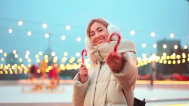 Neşeli kadın, parıldayan ışıklarla süslenmiş canlı bir Noel pazarında gülümserken elinde şeker kamışı tutuyor. Atmosfer neşeli, kış şenliklerinin özünü yakalıyor..