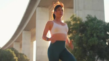 Güneşli bir günde şehir parkında köprü altında koşan sportif kadın koşucudan. Sırtı yanan kadın koşucu dışarıda egzersiz yapıyor.. 