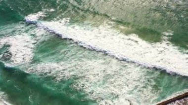 İnsansız hava aracı, sakin okyanus dalgalarını sahildeki kumlu sahile doğru yavaşça yuvarlanırken yakalar. Dalgaların hareketi kıyıya dokunduklarında rahatlatıcı bir etki yaratır. 