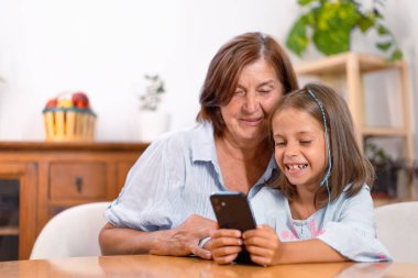 Mutlu torun evde büyükannesinin masasında akıllı telefon kullanıyor. Gülümseyen yüzleri, aletten öğrendikleri ve paylaştıkları şeylerle dolu. 