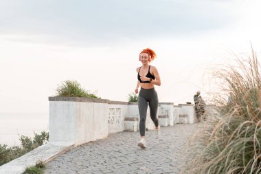 Açık gökyüzüne tepeden bakan kulaklıklarla yaya yolunda koşan kararlı sporcu kadın. Spor giyim kuşağında tüm vücudu gün boyunca koşarken müzik dinleyen bir kadın.. 