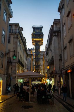 Portugal, Lisbon, 16 january 2023 Elevator de Santa Justa in Baixa in the City of Lisbon in Portugal. Night city lights glow people sit in street restaurants drinking wine clipart