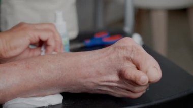 Yaşlı kadın ayağı HALLUX VALGUS ile temizleniyor. Giyinmeye hazırlanırken ayak bakımı ve hijyene odaklanıyor. 