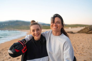 Boks antrenmanından sonra sahilde sarılıp gülen iki gülen arkadaşın portresi. Bir kız eline bir odak eldiveni takıyor, neşe ve dostluk anı yakalıyor.