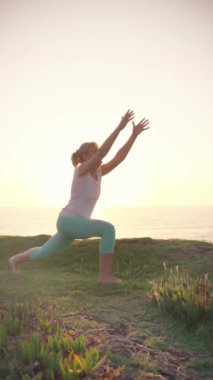 Kadın gün doğumunda plajda hareketli bir yoga pozu veriyor. Sakin atmosferi ve nefes kesici okyanus manzarasını kucaklarken esnekliğini ve gücünü arttırıyor..