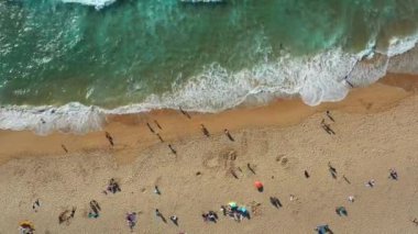 Güneş banyosu yapanlar sıcak kumun ve yumuşak dalgaların tadını çıkarırken drone manzaralı plaj hareketlenmeye devam ediyor. Aileler ve arkadaşlar güneşli bir günde güneşlenmek için toplanırlar..