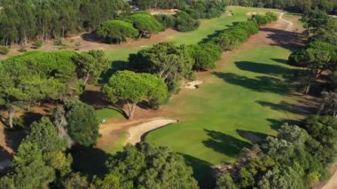 Yükselen ağaçların arasına yuva yapmış, güneşli bir günde zarif bir yerleşim ve canlı yeşillik yakalayan göz kamaştırıcı bir golf sahası..