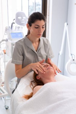 Yüz bakımı. Güzeller güzeli kadın güzellik salonunda serum yağı tedavisi görüyor. Kozmetik uzmanı merkezdeki müşteri şefine kozmetik serumu uyguluyor..