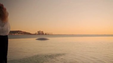 Gün batımında açık gökyüzüne karşı sahilde dans eden neşeli, şehvetli kadın. Güzel genç bayan model doğanın tadını çıkarırken zarif serbest stil hareketler sergiliyor. 