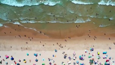 İnsanlar renkli şemsiyeler ve hafif dalgalarla çevrili canlı bir plajda dinleniyor ve oynuyorlar. Sıcak yaz atmosferi ziyaretçileri güneşi emmeye ve kalıcı anılar yaratmaya davet eder.