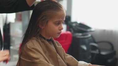 Kuaförde saç tıraşı olan tatlı bir kız. İsimsiz kadın stilisti tarak kullanarak saç stili yaratıyor. Kuaför berber dükkanındaki çocukların saçlarıyla ilgileniyor.