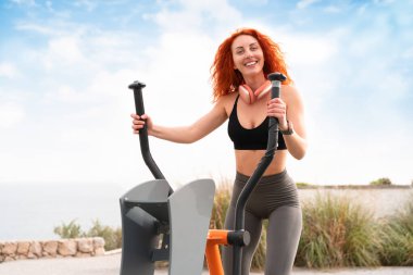 Neşeli, sportif bir kadın spor salonunda stepper makinesiyle egzersiz yapıyor. Spor giysilerinde gülümseyen kadın gündüz vakti parkta egzersiz yapıyor.. 