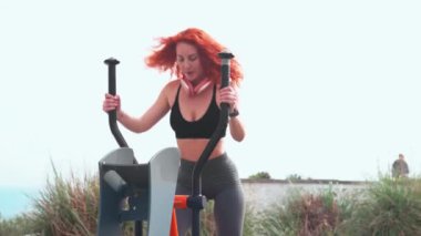 Dalgalı kızıl saçlı sporcu kadın açık havada açık havada spor salonunda stepper makinesinde egzersiz yapıyor. Spor giyim sektöründe genç ve güzel bir bayan gündüz spor yapıyor.