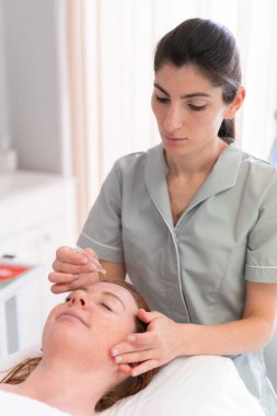 Masaj terapisti kozmetoloji kliniğinde kadın yüzüne serum damlatıyor. Güzel bayan müşteri profesyonel güzellik uzmanları tarafından yüz masajı yaptırıyor.. 