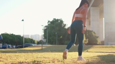 Şehir parkında çömelip saldıran sportif bir kadın. Aktif giyimli kararlı genç bayan sporcu güneş doğarken köprünün yanında egzersiz yapıyor, güç, spor ve sağlıklı yaşam tarzına odaklanıyor.
