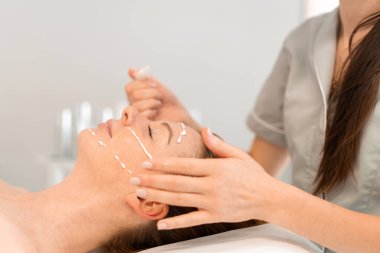 Profesyonel kozmetoloji: Ekin masajı terapisti kuaförde masaj yaparken bir kadına yüz kremi sürüyor. Rahatlamış bayan müşteri spa 'da isimsiz bir güzellik uzmanı tarafından şımartılıyor.