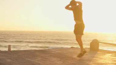 Erkek sporcu vücut egzersizi yapıyor, gün batımında gökyüzünün altında okyanus zeminine doğru ileri doğru hamleler yapıyor. Kafkas fitness meraklısı hamlelere odaklanmış