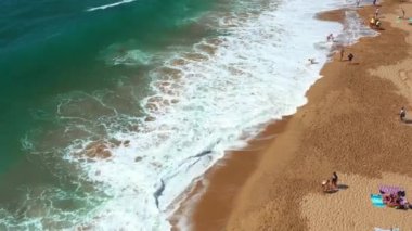 Aileler ve arkadaşlar kıyıda toplanarak, çöken dalgaların altında güneşli bir günün keyfini çıkarırken, kumdan kaleler inşa ediyor ve şemsiyelerin altında dinleniyorlar. Sahile gidenler yaz maceralarının tadını çıkarıyorlar..