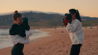 Kararlı kadın boksör gün batımında plajda defansif boks antrenmanı yapıyor ve kadın koç ona rehberlik ediyor. Doğada güçlü genç boksör eğitimi