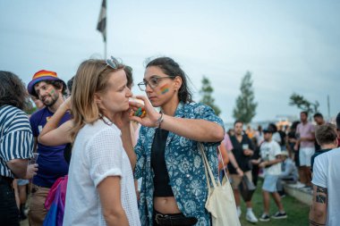 Eşcinsel bir kadın eşcinsel onur yürüyüşü sırasında kız arkadaşının yanağına gökkuşağı bayrağı çiziyor. Erkekler ve kadınlar şehirde LGBTQ haklarını kutluyorlar