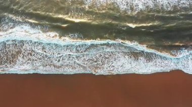 Yumuşak kum ve turkuaz suyla sahile vuran deniz dalgaları, havadan çekilerek huzurlu ve manzaralı sahil manzarası yaratıyor.