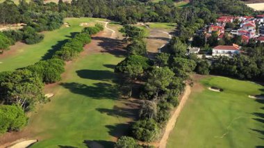 Güneşli bir günde yemyeşil ağaçlarla çevrili golf sahasının hava aracı görüntüsü, dingin bir manzara ve doğal güzellik sergiliyor.