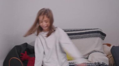 Neşeli kız evde neşeyle dans ediyor, hafta sonları boş zamanlarının tadını çıkarıyor. Güzel çocuk enerjik hareket ediyor, gülümsüyor ve eğleniyor.