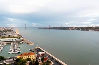 İHA görüntüsü, Lizbon 'daki bulutlu gökyüzüne karşı Tejo Nehri' nin sakin sularını yakalıyor. Endüstriyel ve kentsel yapılarıyla çevreleyen arazi, sakin sularla harmanlanır. 