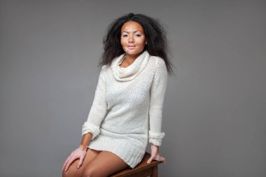Vitiligo cilt hastalığı olan kendine güvenen bir manken gri arka planda, taburede oturuyor. Genç bayanın portresi atölyede beyaz balıkçı yaka kazak giyiyor. 