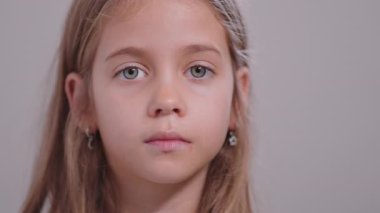 Kameraya yakından bakan ciddi bir kız, odaklanmış bir ifadeyle, basit bir stüdyo arkaplanına bakıyor.