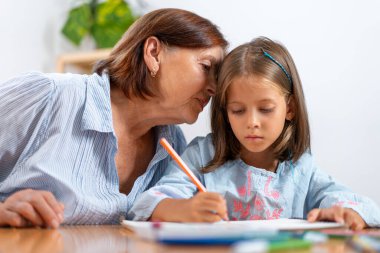 Sevgi dolu büyükanne, torunlarının kulağına gizlice fısıldıyor. Resim, sevgi ve sanatsal aktivitelerle dolu sıcak, sevgi dolu bir anı yakalar. 