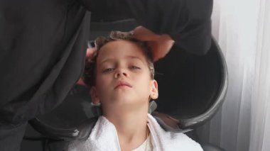 Kuaförde saçlarını yıkayan rahat bir kız. Anonim profesyonel stilist berber dükkanında çocukların saçlarını yıkıyor, düzgün bakım ve tasarım hazırlığı sağlıyor.