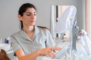 Üniformalı kadın kozmetik uzmanı güzellik kliniğinde LED maske makinesi hazırlıyor. Güzel kadın dermatolog modern bir klinikte tedavi için ekipman kuruyor.