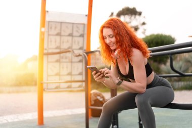 Kızıl saçlı bayan koşucu spor salonunda akıllı telefon kullanıyor. Sportif genç sporcu idmandan sonra cep telefonuyla mesaj atıyor. Gün batımında ayakta dururken cep telefonunda fitness uygulaması kullanıyor.