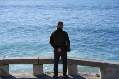 Tanınmayan kıdemli bir adam setin üzerinde tek başına dikilip denizi arkadan izliyor. Duruşu hüznü, yalnızlığı ve yaşlanmanın yalnızlığını yansıtıyor.