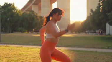 Spor giyimli kararlı bir kadın güneş doğarken köprünün yanında koşuyor. Aktif genç bayan sporcu şehirde spor yapıyor, kondisyon, dayanıklılık ve mercekli sağlıklı yaşam tarzına odaklanıyor.