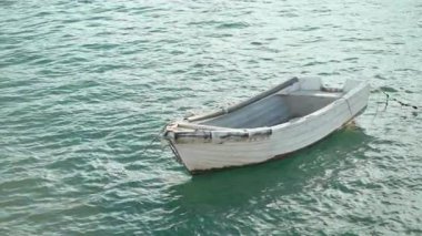 Küçük, yıpranmış tekne sakin sularda yavaşça sürüklenir, sakin kıyı çevresiyle çevrilidir. Huzurlu bir ortam doğanın güzelliğini ve sahildeki yalnızlığı vurgular..