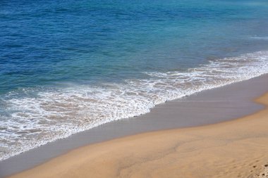 Turkuaz okyanus suyu ve nazik dalgaları olan tropik kumlu bir sahil. Güneşli bir gün, kıyı şeridi boyunca parlak ve huzurlu bir atmosfer yaratır. Rahatlamak için mükemmel bir ortam.