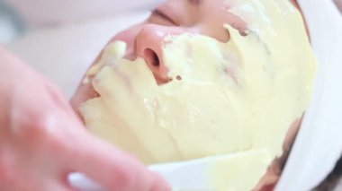 Kimliği belirsiz kadın kozmetolojistin müşterilerin yüzüne sarı alginat maske takarken güzellik salonunda rahat bir yatakta yatarken yakın plan fotoğrafı.