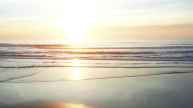 Sakin okyanusun üzerinde altın gün batımı yumuşak kumlu kıyılara doğru süzülürken. Sıcak güneş ışığı suyu yansıtır. Huzurlu bir atmosfer yaratır. Rahatlama ve yansıma için mükemmeldir.