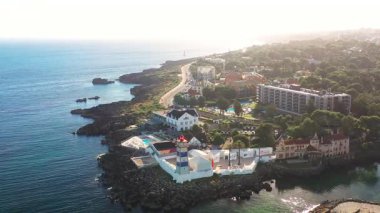 Santa Marta Deniz Feneri 'nin deniz manzaralı insansız hava aracı görüntüleri, yazları Cascais, Portekiz' de güneşli gökyüzü altında kayalık sahil şeridini ve marinayı gösteriyor.