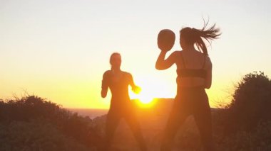 Gün batımında tepede boks antrenmanı yapan sportif kadın boksör. Kadın antrenör ona rehberlik ediyor. Manzaralı plaj ortamında kararlı boksör eğitimi