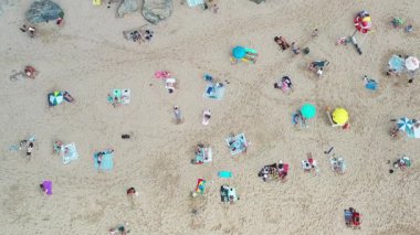 İnsanlar kumlu sahilde renkli şemsiyelerle dinlenirken dalgalar sahile çarpıyor. Hava manzarası, turistlerin güneş ve deniz melteminin tadını çıkardıkları plajda canlı bir yaz manzarası yakalıyor.